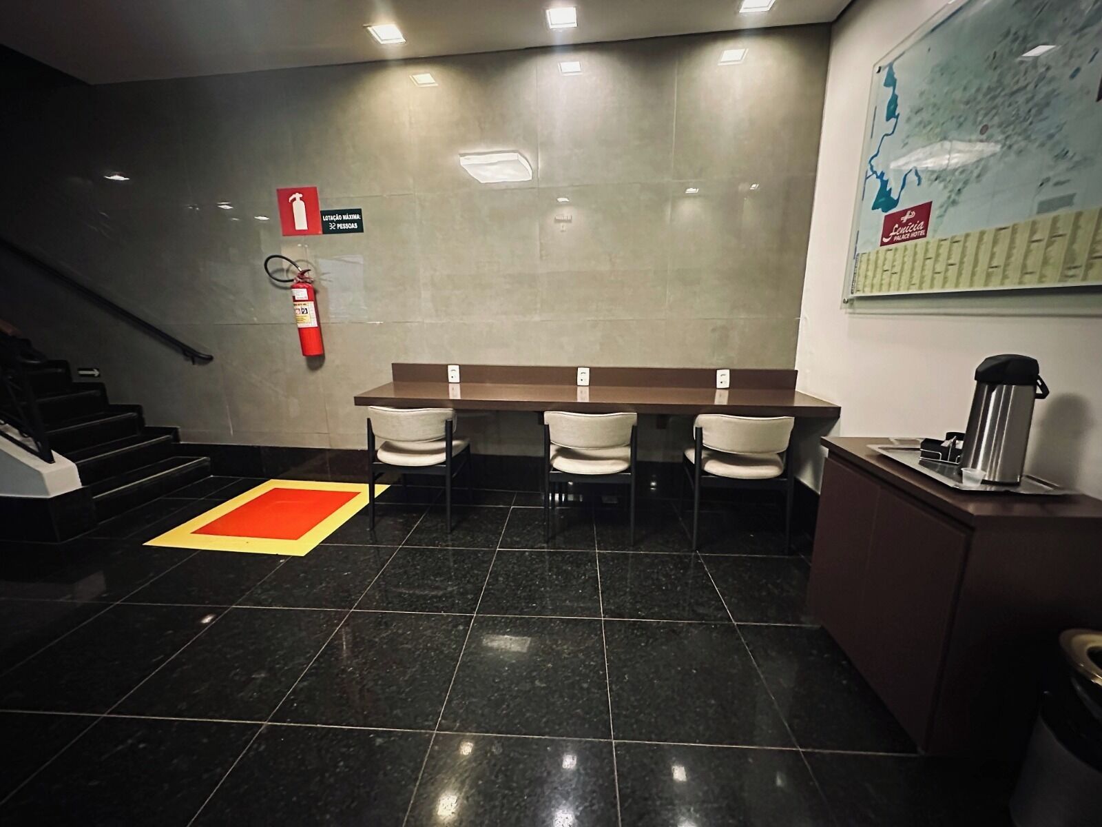 Et hotel lobby med en receptionsdisk, tre stole, en brandslukker og et kort på væggen.