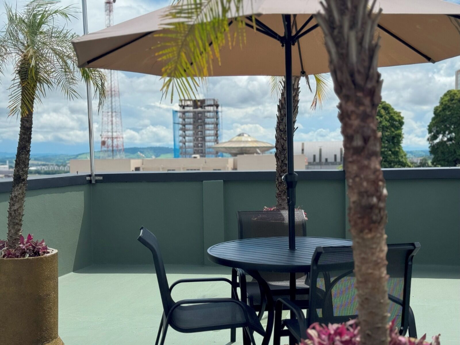 Una terraza en la azotea con mesa y sillas, una sombrilla grande y plantas en macetas.