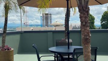 Una terraza en la azotea con mesa y sillas, una sombrilla grande y plantas en macetas.