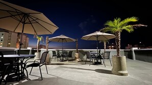 Een terras met tafels en stoelen, parasols en palmbomen.