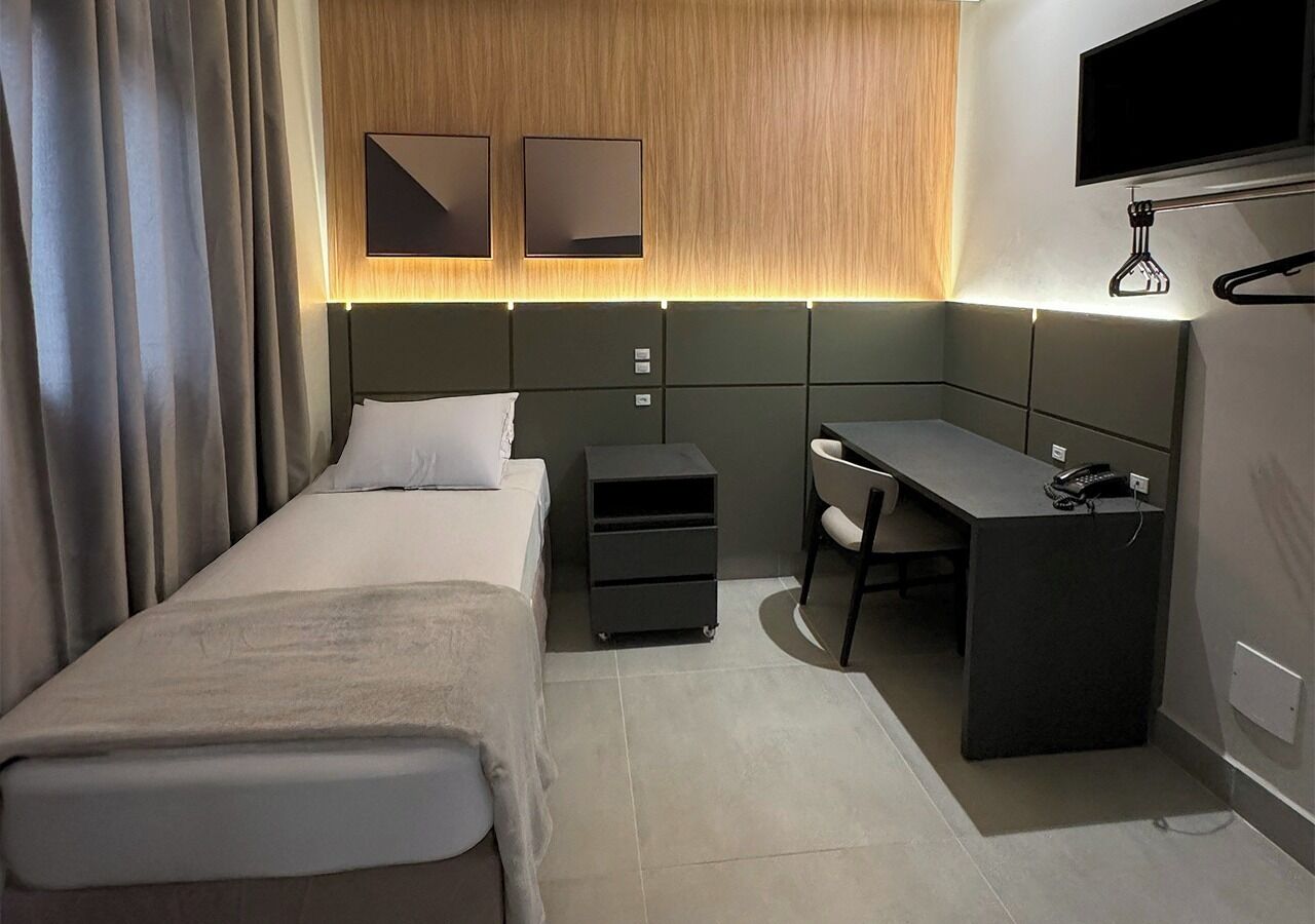 A modern hotel room with a bed, desk, and a TV mounted on the wall.