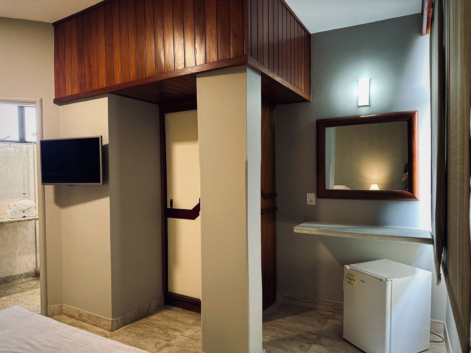 Een hotelkamer met een televisie, een spiegel, een kleine koelkast en een houten plafond.