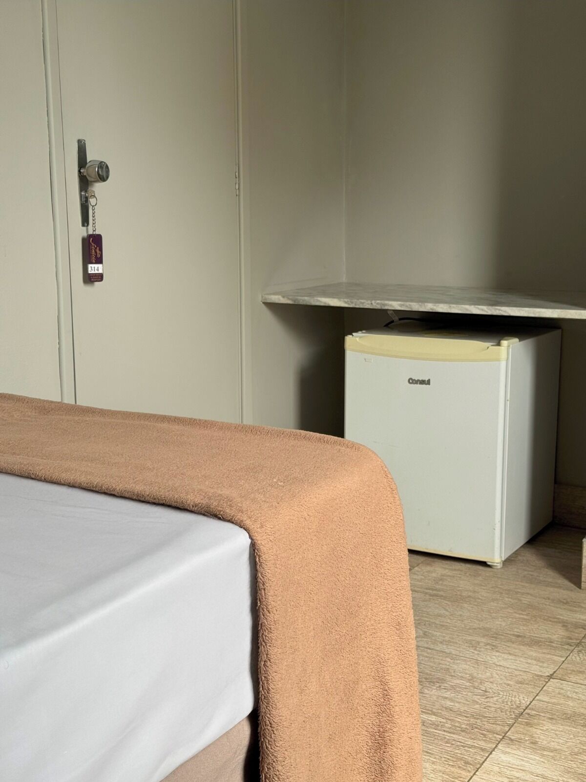 Une chambre d’hôtel avec un lit, un minibar et une porte fermée à clé.