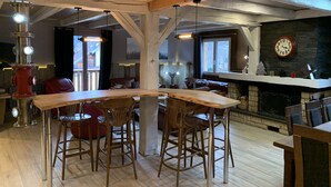Un interior acogedor con techo de madera, una zona de bar con taburetes, chimenea y un reloj en la pared.