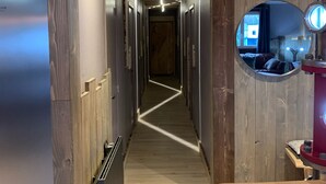 Un pasillo estrecho con paredes y suelo de madera, que lleva a una habitación con cama y ventana.