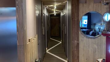 Un couloir étroit aux murs et au plancher en bois, qui mène à une pièce contenant un lit et une fenêtre.