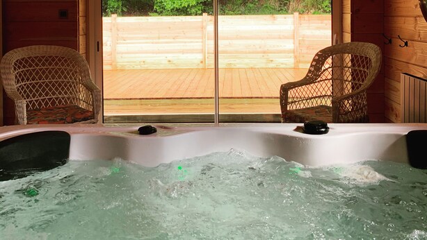 Una cabaña de madera con un jacuzzi, dos sillones de mimbre y vistas a una terraza de madera y vegetación.