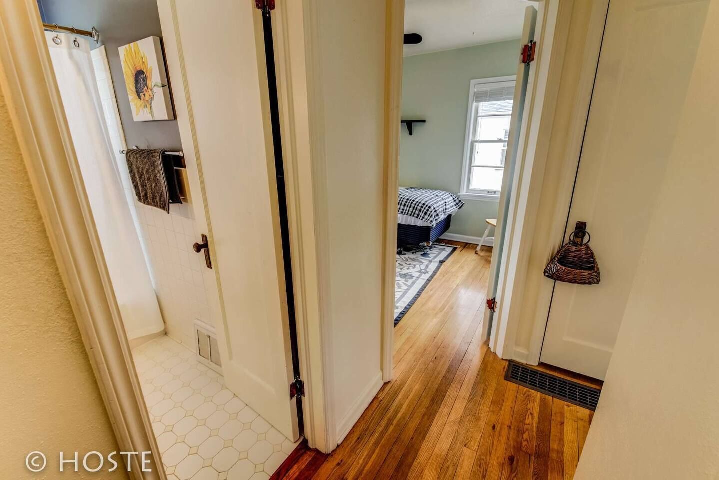 A hallway leading to a bedroom with a bed, a window, and a wall-mounted basket.