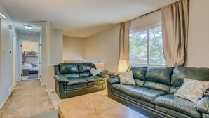 A living room with two leather sofas, a wooden coffee table, and a lamp. A bunk bed is visible in the background.