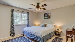 A bedroom with a bed, bedside tables, a ceiling fan, a window with curtains, and a rug.