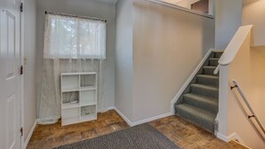 A staircase with a carpeted landing, a white shelf unit, and a window with sheer curtains.