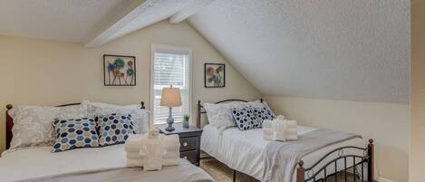 A bedroom with two beds, a window with blinds, and a ceiling with a sloped design.