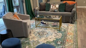 Een woonkamer met een grijze bank, een bijzettafeltje en een kamerbreed tapijt.