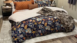 Een slaapkamer met een houten hoofdbord, een bed met bloemenbeddels, een nachtkastje met een lamp en een plafondventilator.