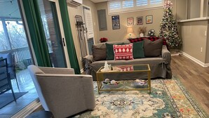 Een gezellige woonkamer met een bank, salontafel en poefs. Een kerstboom en kerstdecoraties zijn zichtbaar.