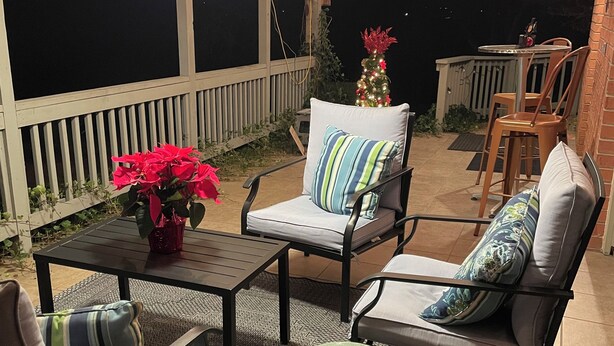 Een overdekt terras met buitenmeubilair, een kerstboom en lichtjes.