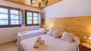 A hotel room with two beds, wooden headboard, large windows, and a chandelier.