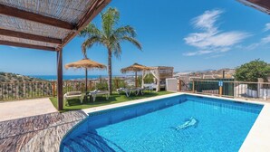 A swimming pool with lounge chairs and palm trees, overlooking a coastal landscape.