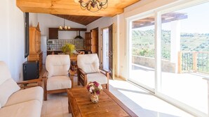 A spacious living area with a wooden ceiling, a dining table with chairs, and a view of the outdoors through large windows.