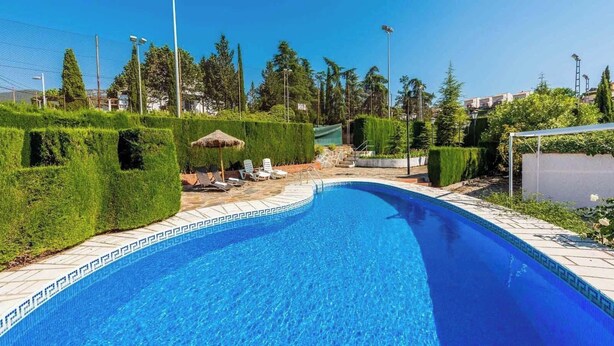 Piscina com borda azulejada, rodeada por sebes bem aparadas e alguns cadeões de descanso.
