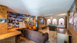 Um espaço interno aconchegante com mesa de bilhar, sofá e parede decorada com fotografias.