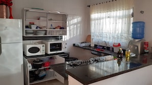 Une cuisine équipée d’un réfrigérateur, d’un four à micro-ondes, d’une cuisinière et de divers ustensiles de cuisine rangés sur des étagères.