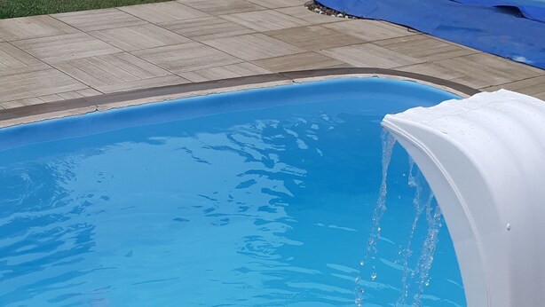 Une piscine à l’eau cristalline et d’un bleu éclatant, agrémentée d’une fontaine à eau blanche.
