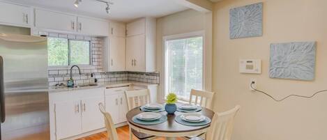 A modern kitchen with white cabinets, a stainless steel refrigerator, and a dining area with a round table and chairs.