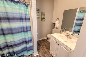 A bathroom with a shower curtain, toilet, sink, and mirror. - 3BR Of Downtown King Bed, Dining, Has It All! (Colorado Springs)