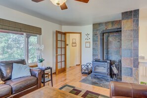 A living room with a fireplace, leather sofa, wooden flooring, and a ceiling fan. - 4 BR Country Home in Suburbs W/trails & Parks (Colorado Springs)