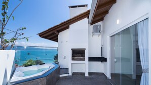 A balcony with a hot tub, a grill, and a glass door leading to a pool area. - pousada solar das tartarugas (Bombinhas)