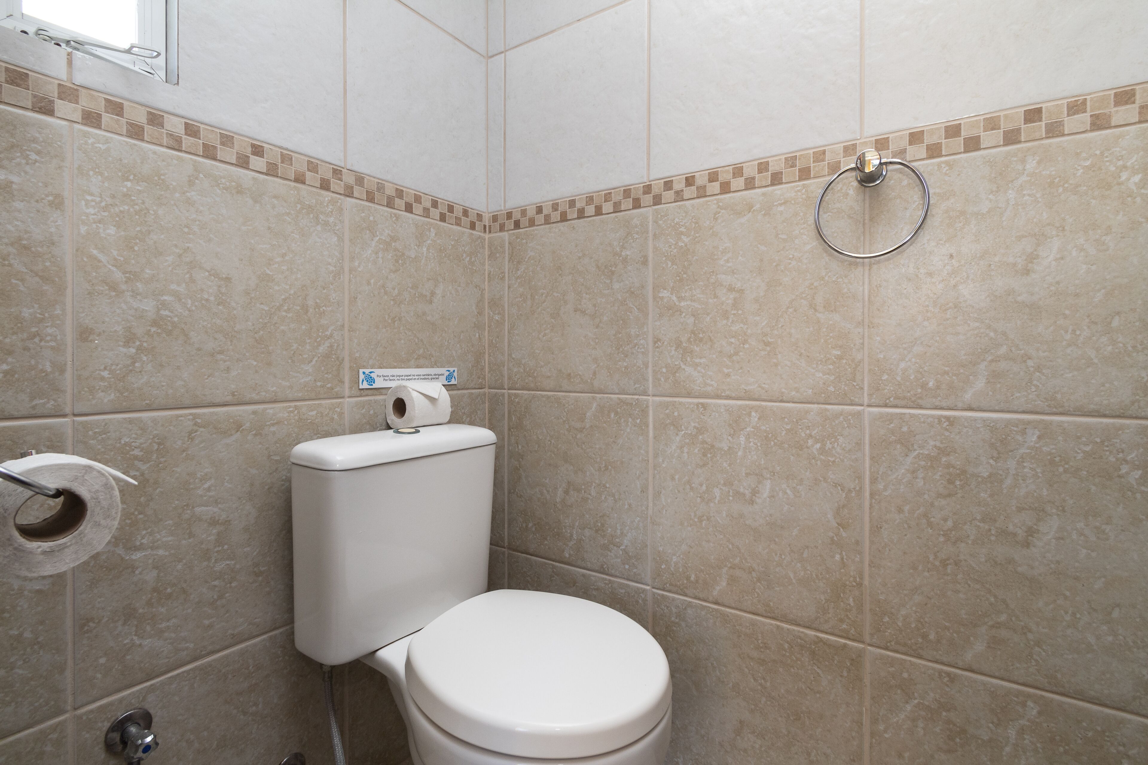 A bathroom with a toilet, a towel ring, and a roll of toilet paper.