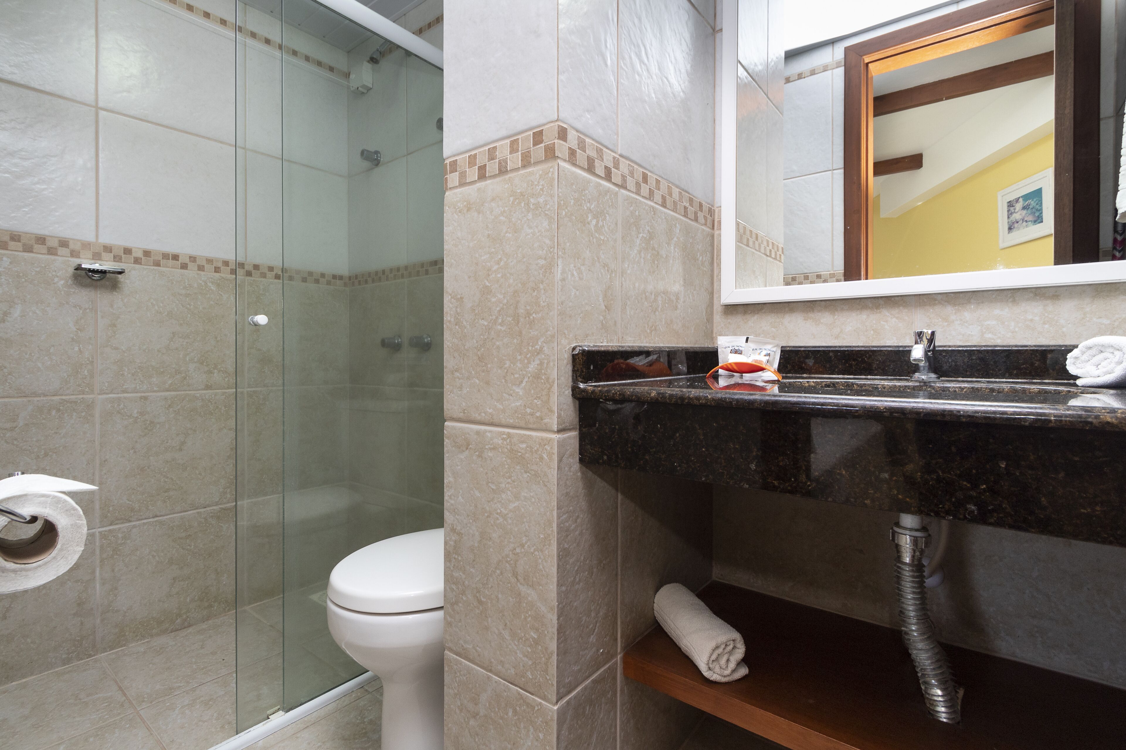 A bathroom with a glass-enclosed shower, a white toilet, and a black sink with a towel on the counter.