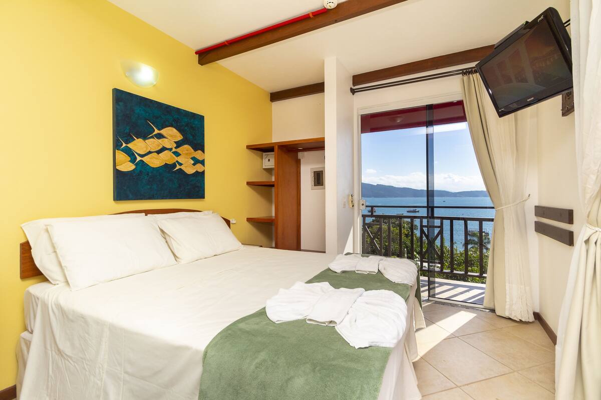 Une chambre d’hôtel avec un lit, un plaid vert, un tableau au mur, une télévision et un balcon avec vue.