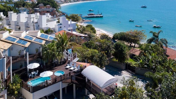 A coastal hotel with a pool, sun loungers, and a view of the sea. - pousada solar das tartarugas (Bombinhas)