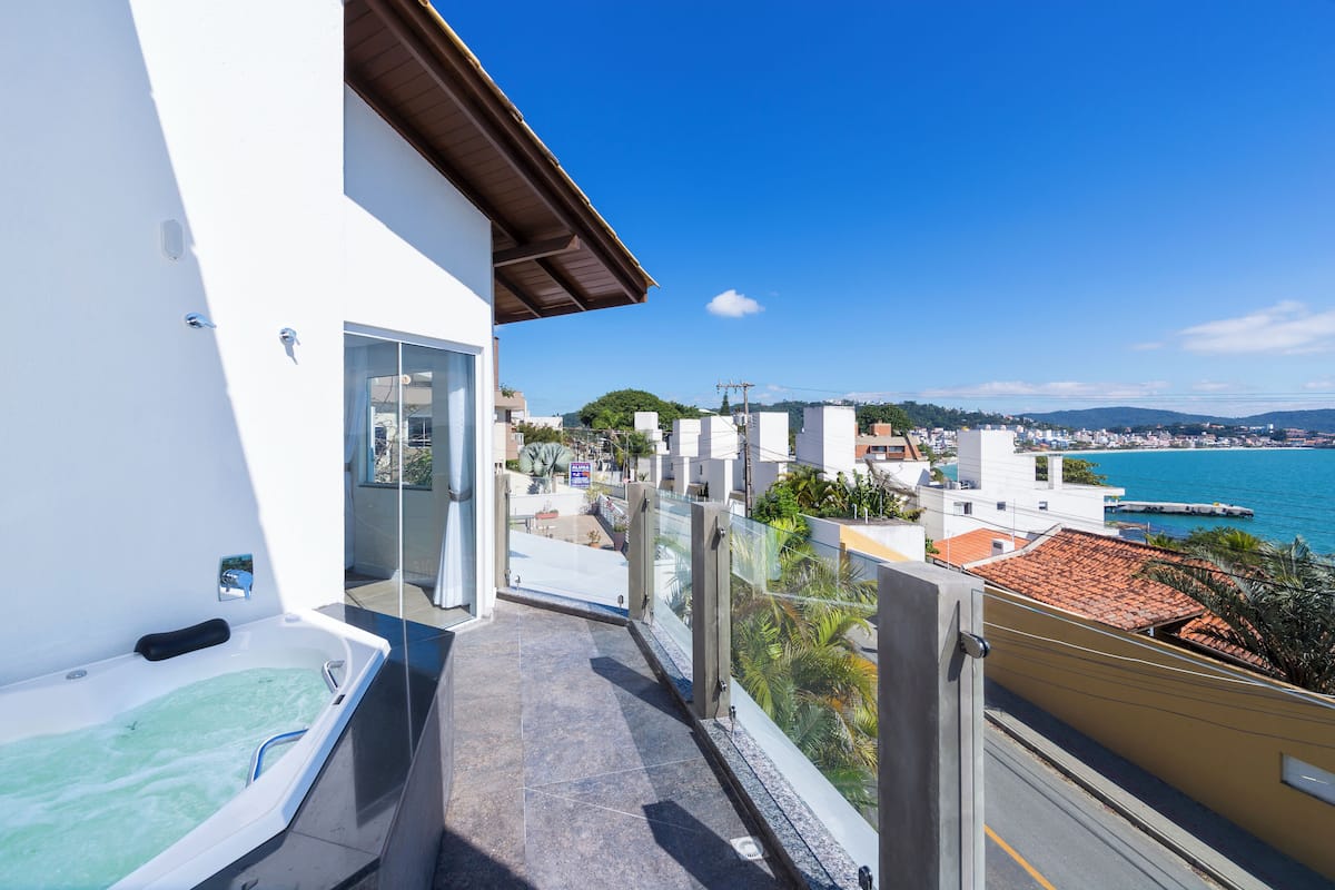 Un balcon avec un jacuzzi, une vue dégagée sur la mer et un paysage urbain en arrière-plan.