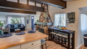 A cozy kitchen with a stone fireplace, wooden beams, a dining table with chairs, and a living area with a sofa and curtains. - 2brcheyenne Cañon Minutes to Hiking and Zoo (Colorado Springs)