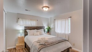 A bedroom with a wooden bed frame, a bedside table with a lamp, a potted plant, and a window with curtains. - 2brcheyenne Cañon Minutes to Hiking and Zoo (Colorado Springs)