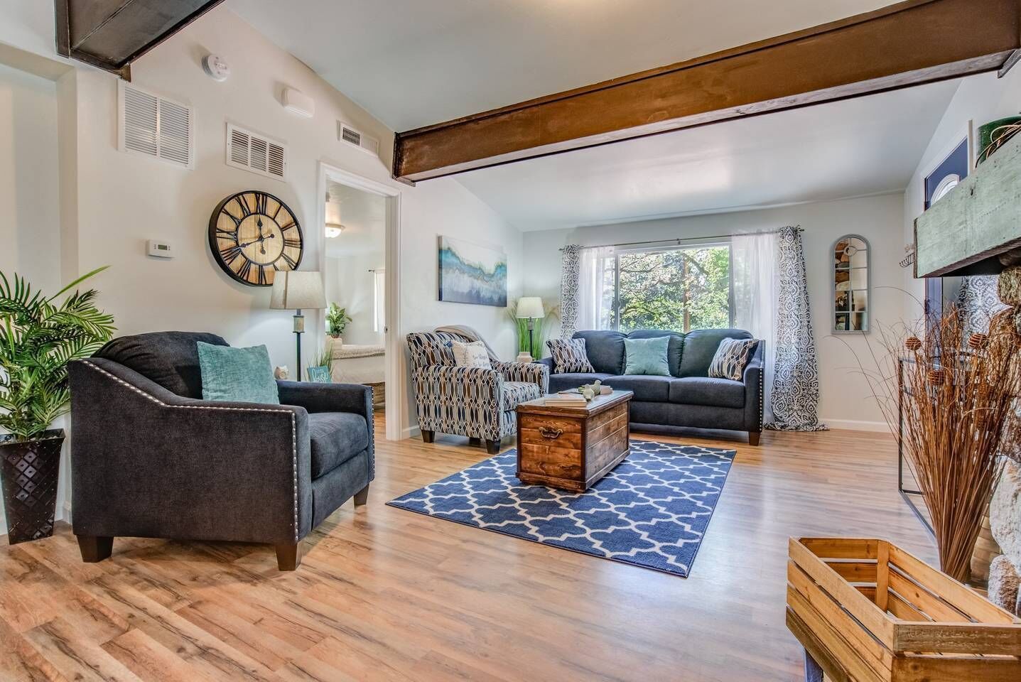 A spacious living room with a large clock, a wooden coffee table, and a patterned rug.