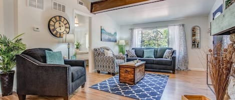 A spacious living room with a large clock, a wooden coffee table, and a patterned rug.