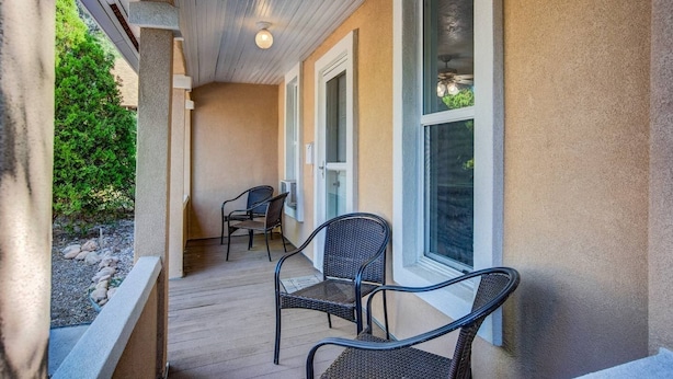 A covered porch with two wicker chairs, a small table, and a window with a view of greenery.
