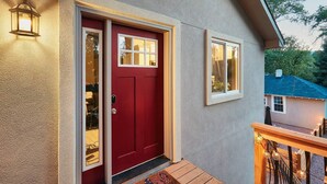 A red door with a glass panel, a small window above it, and a light fixture on the wall.
