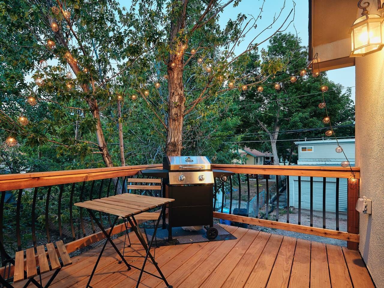 A wooden deck with a barbecue grill and a table, surrounded by trees and a railing.