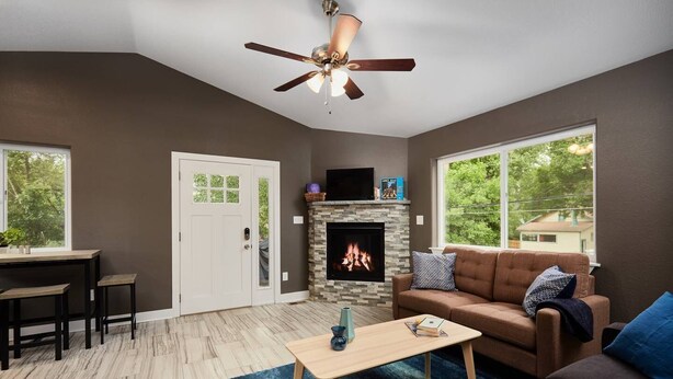 A living room with a fireplace, a ceiling fan, a sofa, a coffee table, and a dining area with chairs.