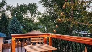 A wooden deck with a table and chairs, surrounded by trees and a building in the background.