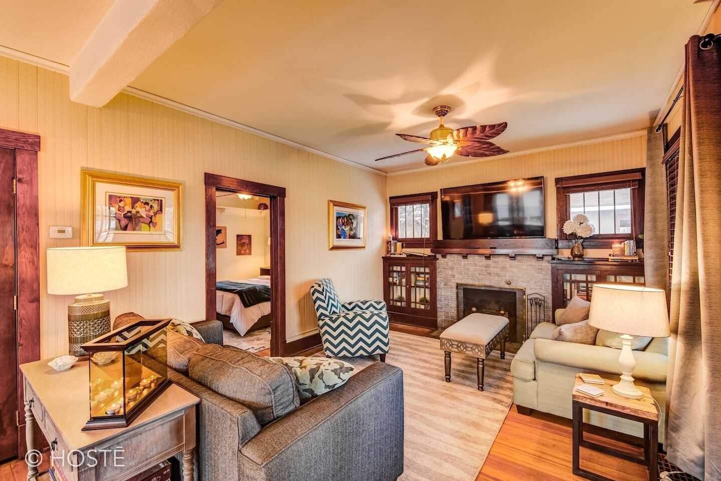 A cozy living room with a fireplace, a ceiling fan, and a television.