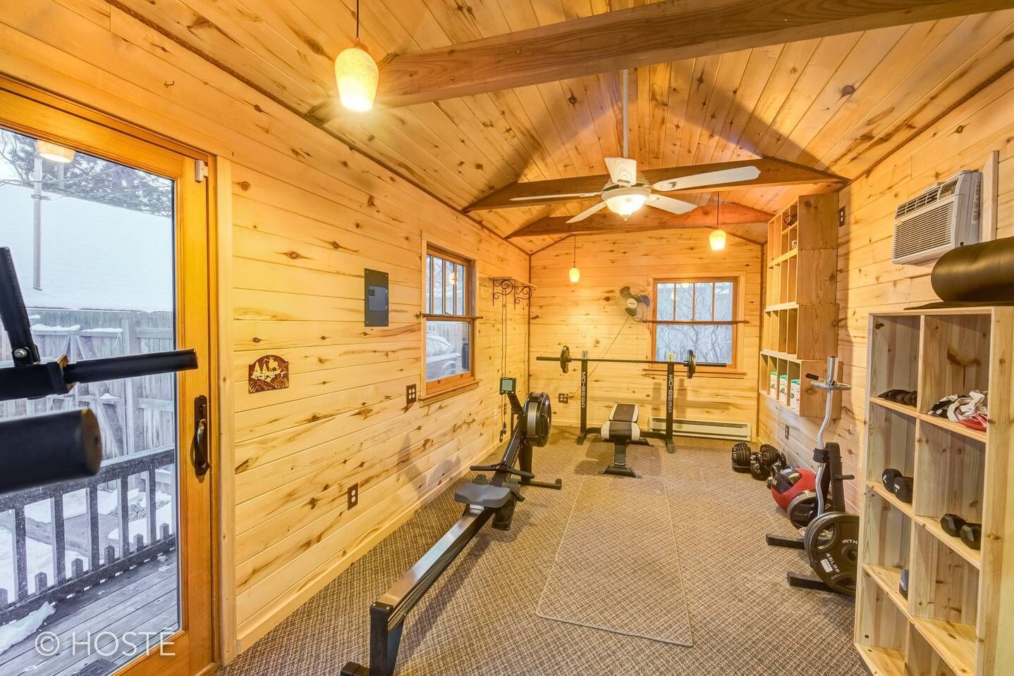 Une cabane en bois dotée d’un espace de remise en forme comprenant du matériel d’exercice et un ventilateur de plafond.