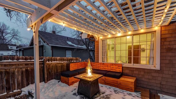 A covered patio area with a fire pit, wooden seating, and string lights. - 4BR Dog Friendly Mtn Retreat With Gym! (Colorado Springs)