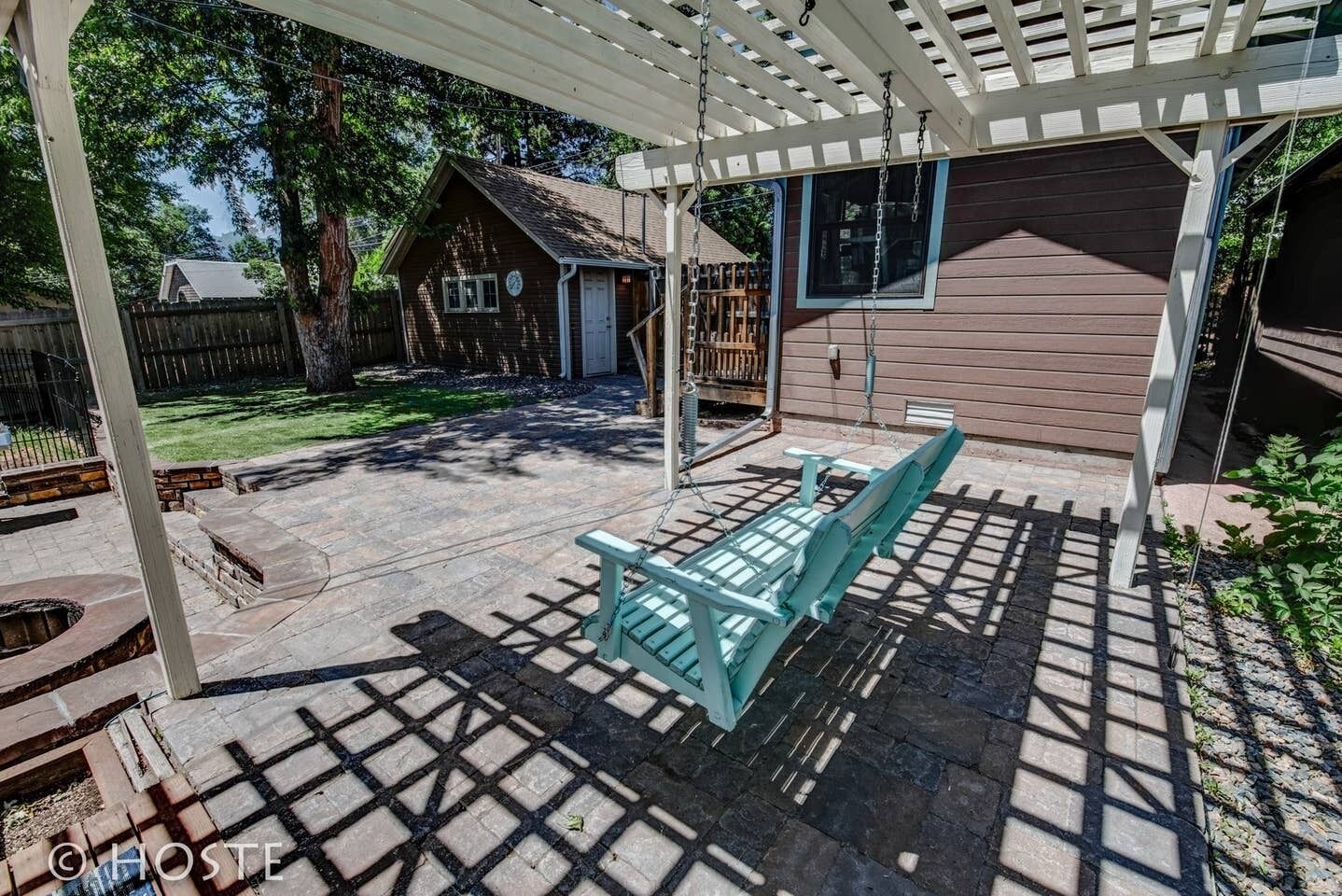 Eine überdachte Terrasse mit Schaukeln, ein Holzhaus und ein durch Zäune umfriedetes Grundstück.