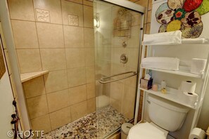 Een badkamer met een douche met glazen wand, een toilet en een plank met handdoeken en toiletartikelen.